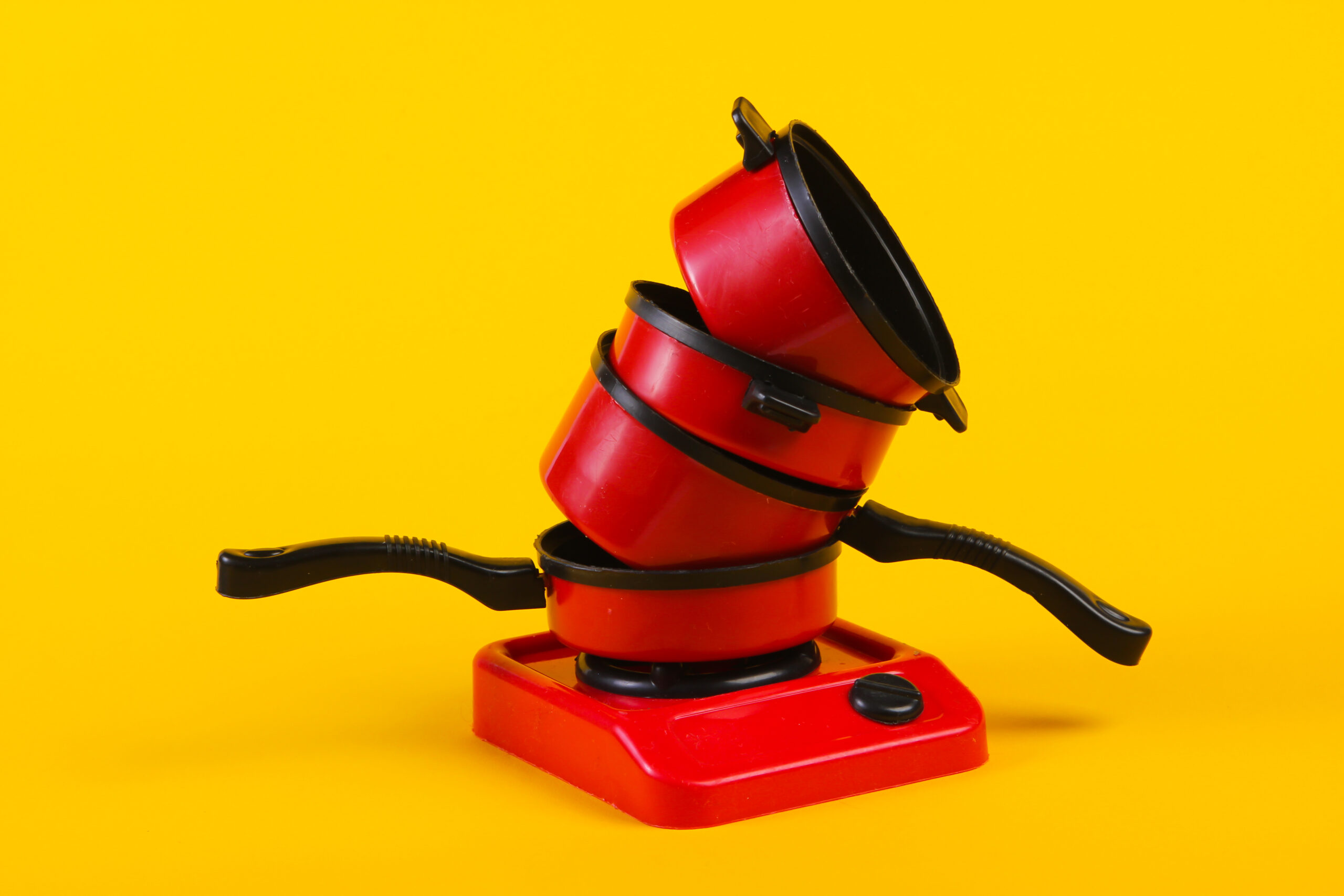 Toy plastic stove with stack of pans on yellow background. Kid’s Kitchen Toy plastic stove with stack of pans on yellow background. Kid's Kitchen